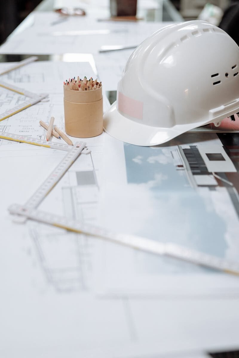 A detailed view of an architect's desk with plans, a hard hat, and drafting tools.