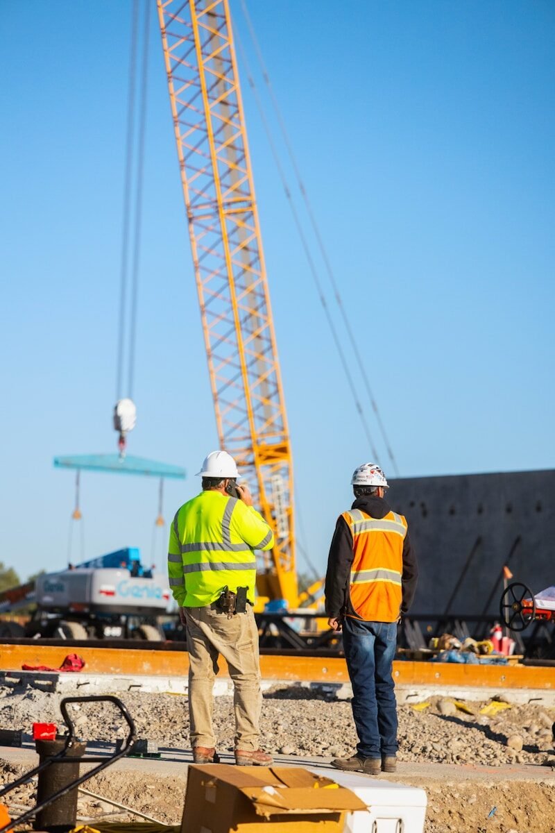 Construction workers observe a crane lifting materials.